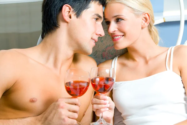 Joven feliz pareja amorosa celebrando con vino tinto en el dormitorio —  Fotos de Stock