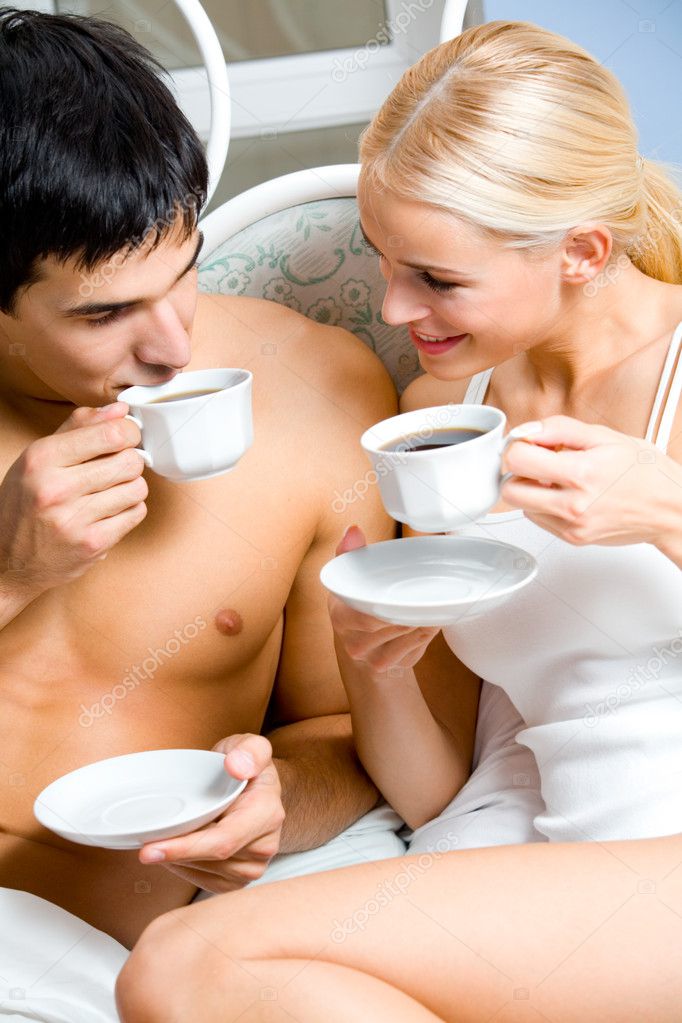 Young happy smiling couple drinking coffee at bedroom