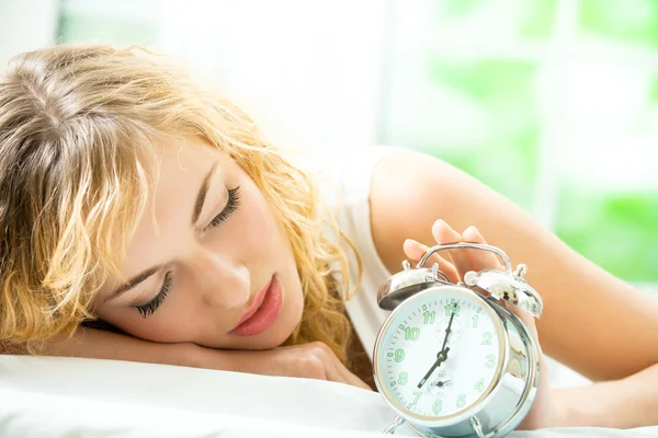 Žena s alarmclock ležící na posteli, doma — Stock fotografie