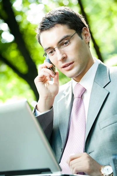 Homme d'affaires travaillant avec ordinateur portable et téléphone portable, à l'extérieur — Photo