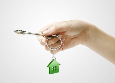 Hand holding key with a keychain in the shape of the house. clipart