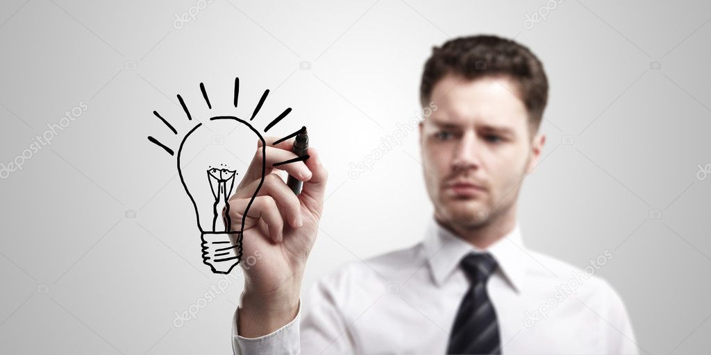 Young business man drawing a light bulb on a glass screen with black marker