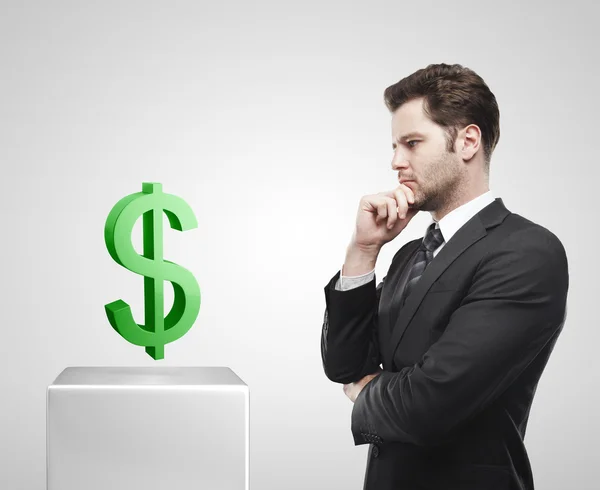 Jovem empresário olha para o sinal verde do dólar americano em um pedestal branco . — Fotografia de Stock