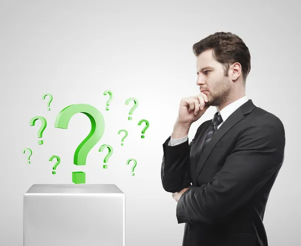 Giovane uomo d'affari guarda i punti interrogativi verdi su un piedistallo bianco . — Foto Stock