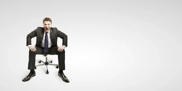 Young businessman shouting and sitting on a chair. — Stock Photo, Image