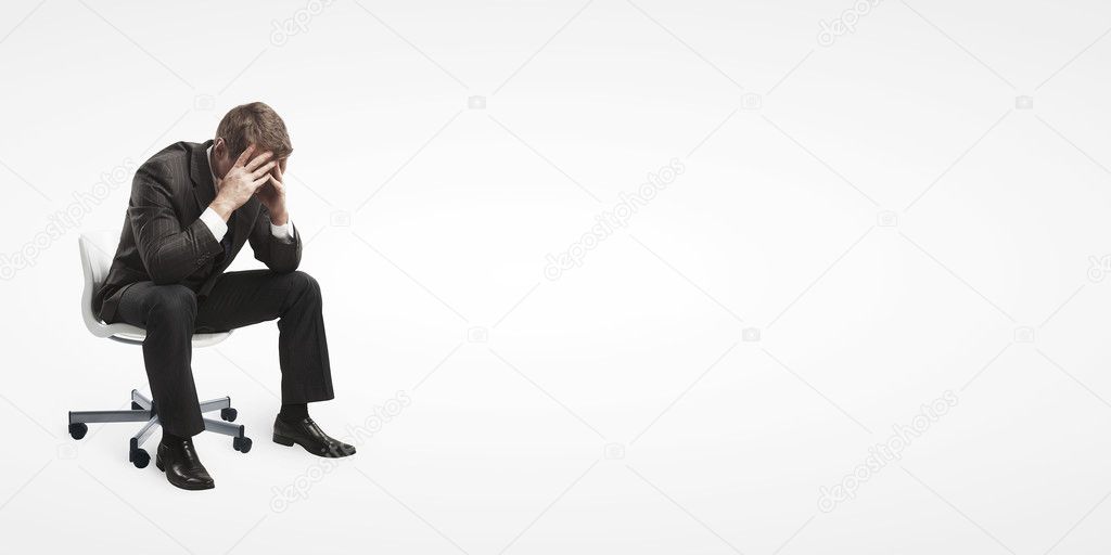 Young businessman sitting on chair with head down as if sad or depressed.