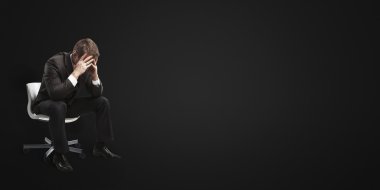 Young businessman sitting on chair with head down as if sad or depressed. clipart