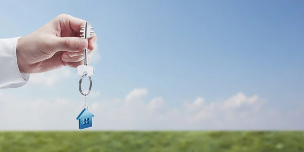 Ruka drží klíč s klíčenka ve tvaru domu. — Stock fotografie
