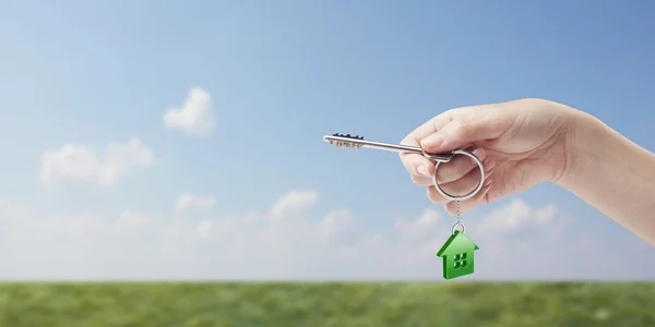 Hand som håller nyckel med en nyckelring i form av huset. — Stockfoto