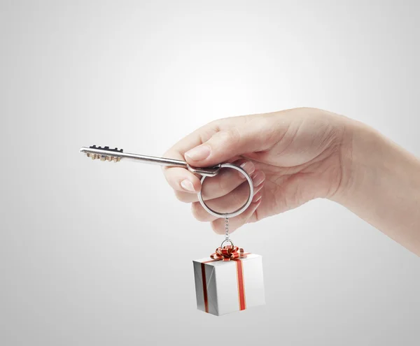 Χέρι που κρατά το κλειδί με ένα μπρελόκ σε σχήμα το κιβώτιο δώρων. — Φωτογραφία Αρχείου