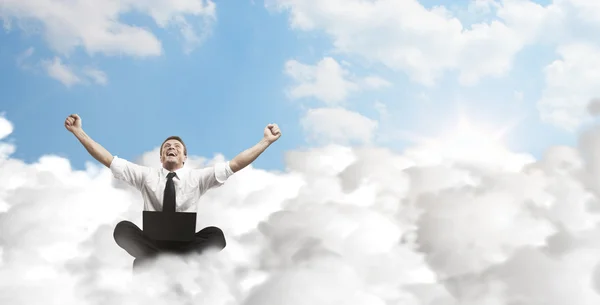 Heureux jeune homme d'affaires avec ordinateur portable assis sur les nuages . — Photo