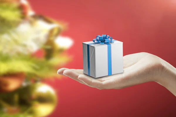 Caja de regalo en una mano femenina. Sobre un fondo rojo . —  Fotos de Stock