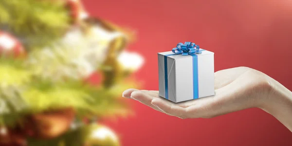 Geschenkbox auf einer weiblichen Hand. auf rotem Hintergrund. — Stockfoto