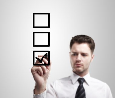 Young business man drawing a tick on a glass window in an office clipart