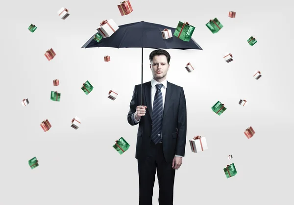 Junger Geschäftsmann mit Regenschirm unter Geschenkboxen regen. — Stockfoto