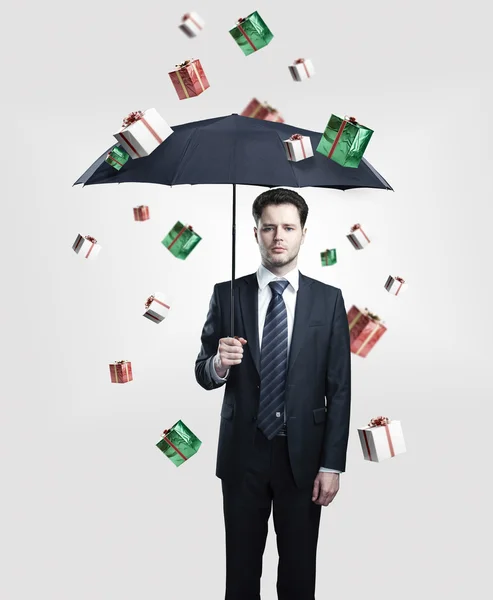 Jonge zakenman met paraplu onder geschenk dozen regen. — Stockfoto
