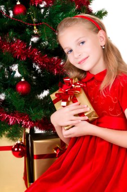 Young girl with gift sit near Christmas tree. clipart