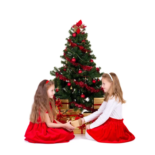 Zwei kleine Mädchen sitzen am Weihnachtsbaum. — Stockfoto