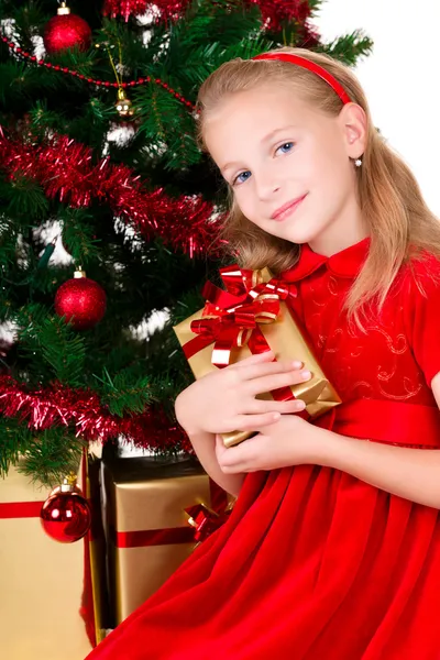 Ung flicka med gåva sitta nära julgran. — Stock fotografie