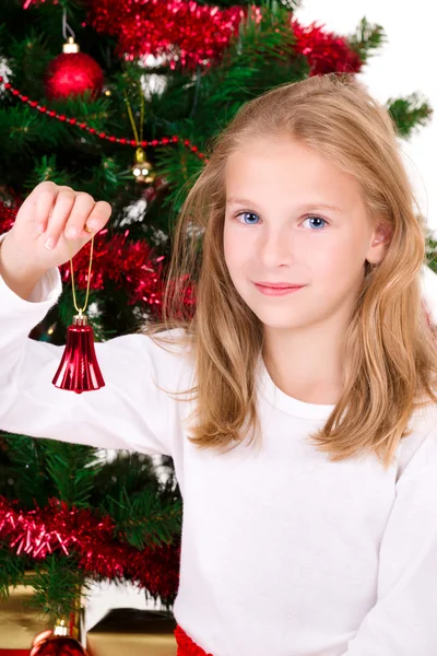 Ung flicka med bell sitta nära julgran. Stockfoto