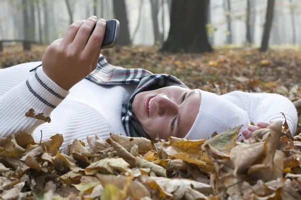 Joven con sonrisa y teléfono móvil en otoño —  Fotos de Stock