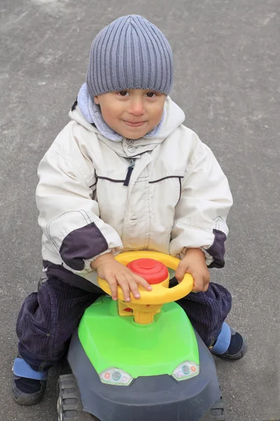 Улыбающийся мальчик за рулем игрушечной машины — стоковое фото