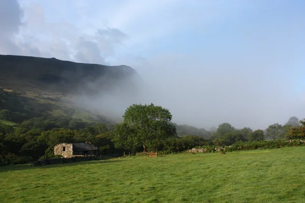 Niebla rodando por un valle oscureciendo una montaña — Foto de Stock