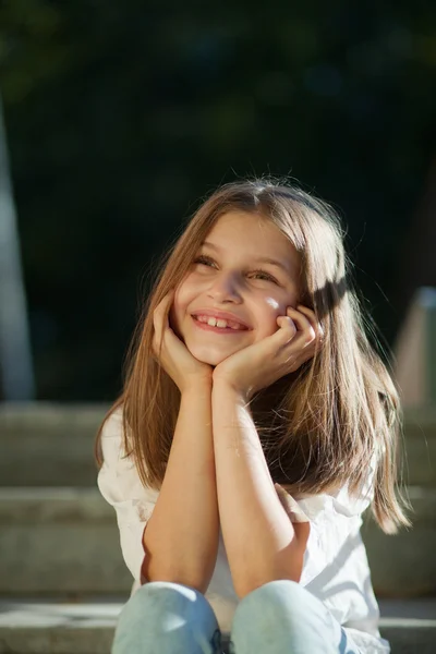 Κορίτσι κάθεται συγκρατείται στο κεφάλι με τα χέρια του και χαμογελαστός — Φωτογραφία Αρχείου