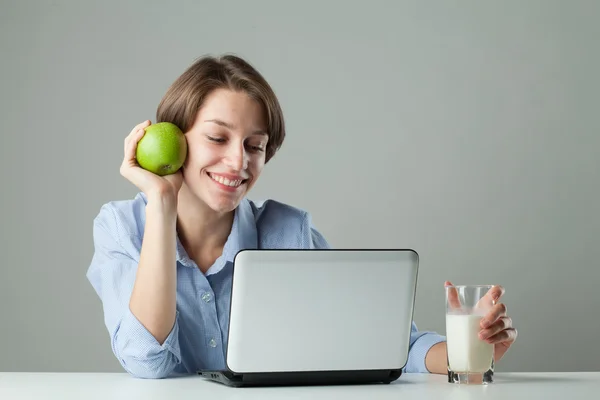 Chica en la mesa con un portátil en un vaso de leche y una manzana —  Fotos de Stock