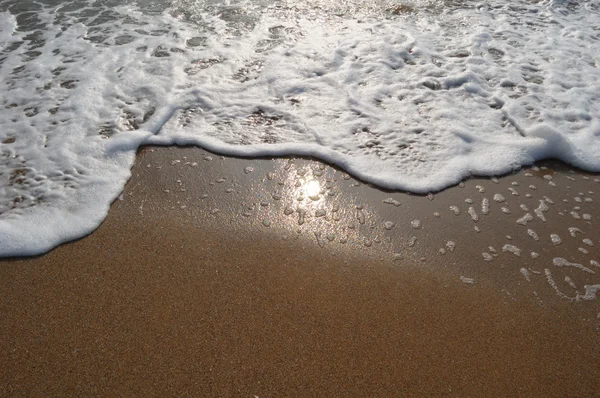Las olas del mar y la espuma blanca en la playa de arena con el sol reflejan — Foto de Stock
