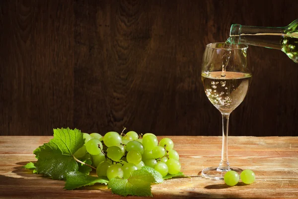 stock image White wine pouring down to the glass with grapes