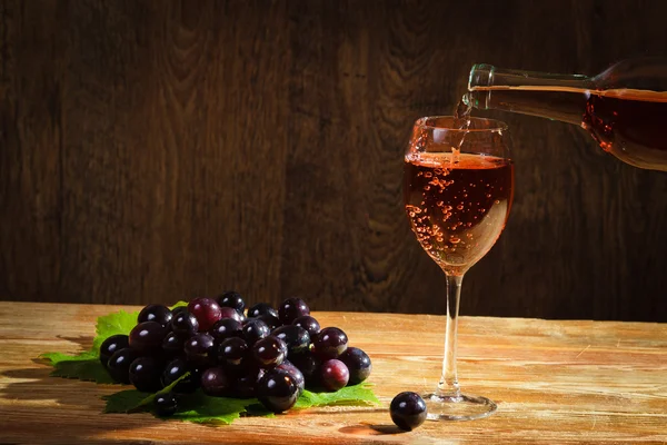 Red wine pouring down to the glass with grapes — Stock Photo, Image