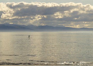 Stand up paddle surfer in calm water at dusk with dramactic clou clipart