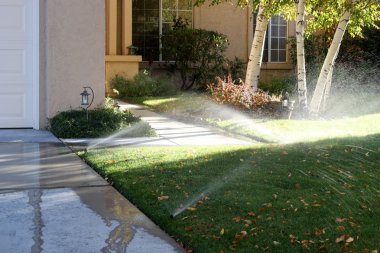 Sprinklers running onto the sidewalks of a typical American trac clipart