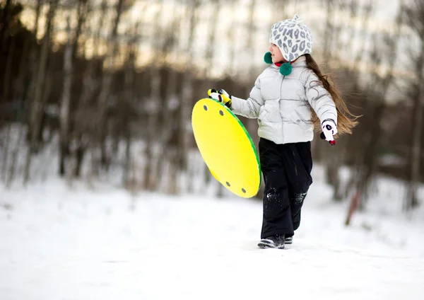 Χαριτωμένο μικρό κορίτσι που τρέχει στο χιόνι με πιατάκι — Φωτογραφία Αρχείου