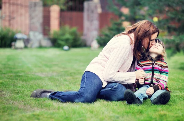 Young mother kisses her daughter on the lawn — Stock Photo, Image