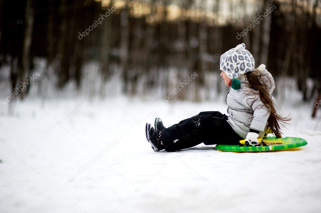 Adorable child girl sledding in snow on a saucer