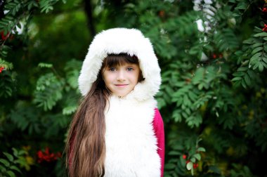 Cute little girl in fur coat under rowan tree clipart