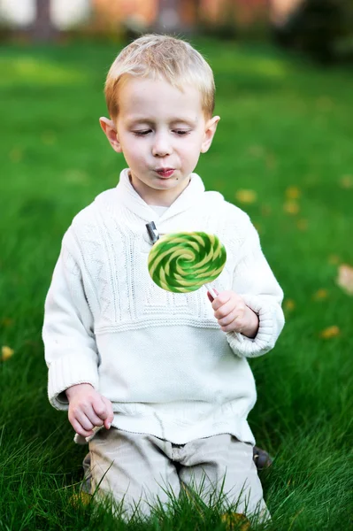 Niño pequeño con gran piruleta en un césped verde —  Fotos de Stock