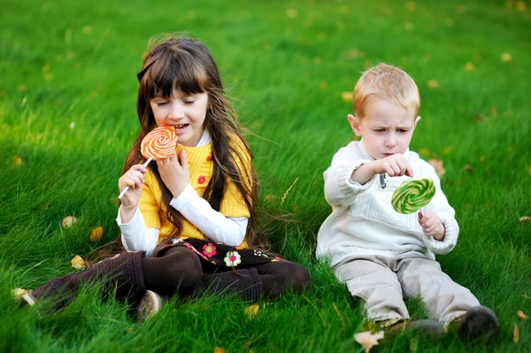 Mali przyjaciele jeść lizaki razem na trawnik — Zdjęcie stockowe