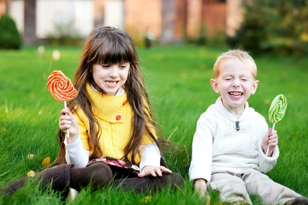 Malí přátelé společně jíst lízátka na trávníku — Stock fotografie
