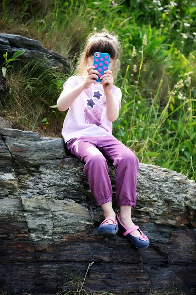 Little girl with mobile phone on rocks — Stock Photo, Image