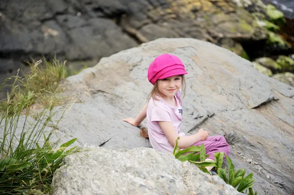 Glückliches kleines Mädchen mit rosa Sonnenhut auf den Felsen — Stockfoto