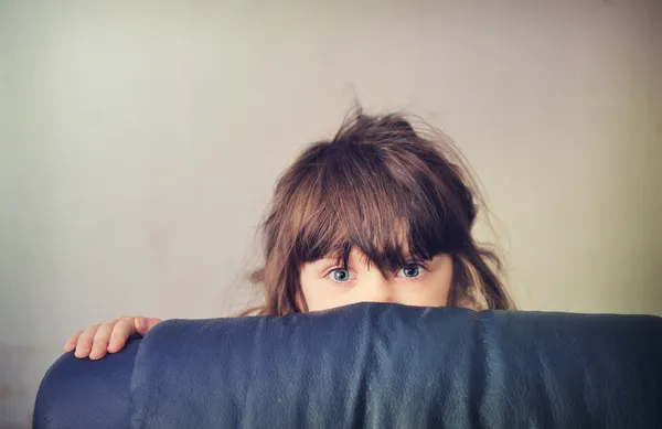 Liten flicka som leker kurragömma bakom soffan — Stockfoto