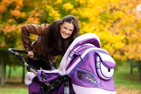 Young mother with baby in stroller walks in park — Stock Photo, Image