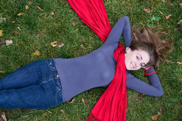 Morena bela mulher está em cachecol vermelho deitado na grama . Fotos De Bancos De Imagens Sem Royalties