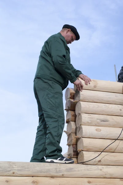 Carpintero en la pared de la cabaña de madera en construcción — Foto de Stock