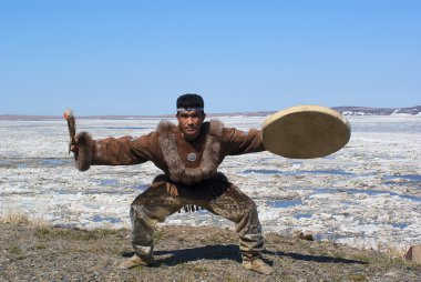 Chukchi man dancing a folk dance against spring landscape clipart