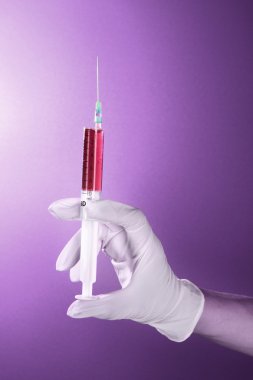 Syringe with blood in the doctor's hand on the purple background clipart