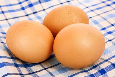 Three brown hen's eggs on the blue chequered cloth clipart